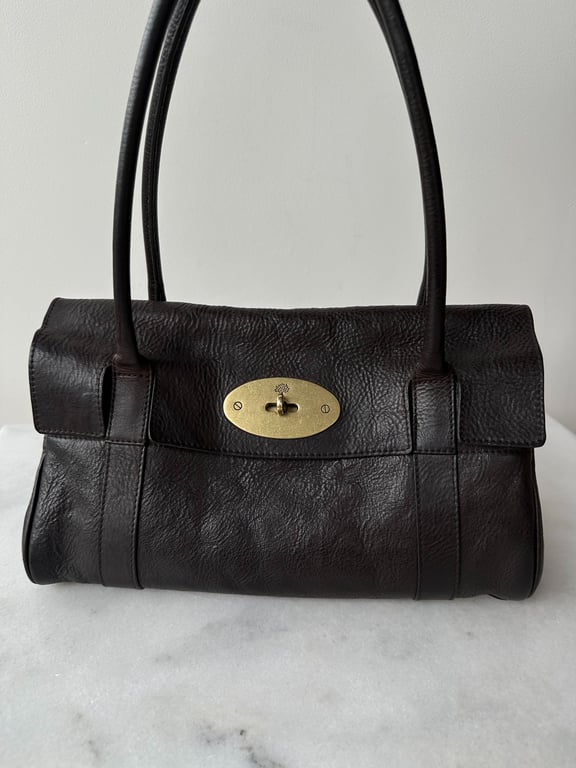 Sort læderhåndtaske med dobbelte håndtag og en oval, guldfarvet drejelås på forsiden.