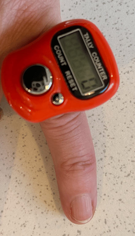 En rød digital tæller på en finger mod en lys, marmoreret bordplade.