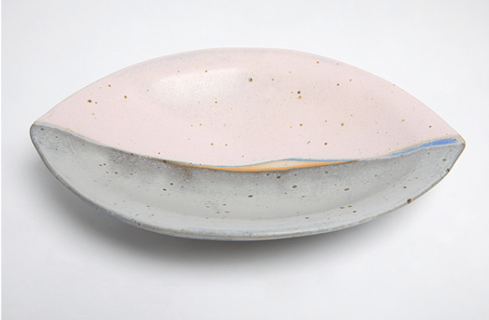 En keramisk skål med en oval form, hvid med små brune og blå pletter, og en glat, blank overflade.