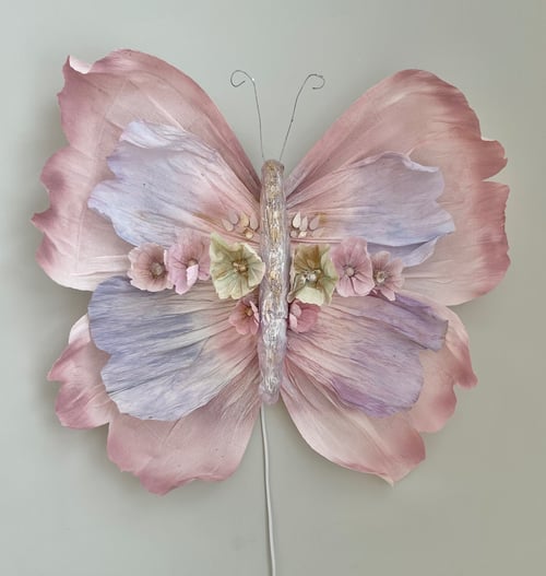 Stor sommerfugl lavet af pastelfarvede blomsterblade og fine blomsterdetaljer, monteret på en væg. (1)