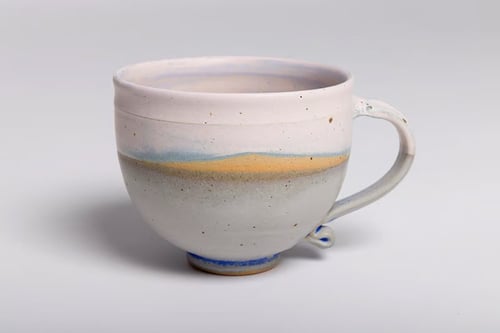 Keramisk kop med håndtag, dekoreret med blå, gul og grå nuancer på en hvid baggrund.