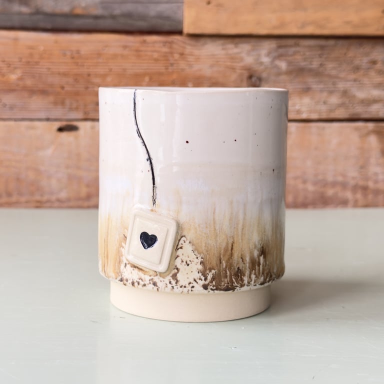 Keramikkop med brune og hvide nuancer, dekoreret med en lille firkantet "tepose" med et sort hjerte.