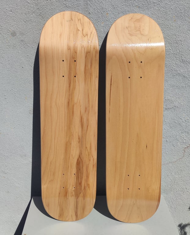 To tomme skateboard decks i lyst, naturligt træ, placeret lodret mod en grå betonvæg.