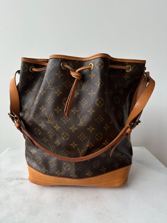 Brun Louis Vuitton skuldertaske i læder med monogrammønster og justerbar rem, placeret på marmorbord mod en neutral baggrund.
