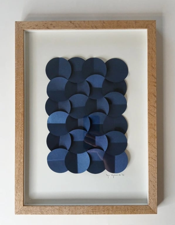 Tegning af overlappende, foldede cirkler i blå nuancer indrammet i en simpel træramme. (2)