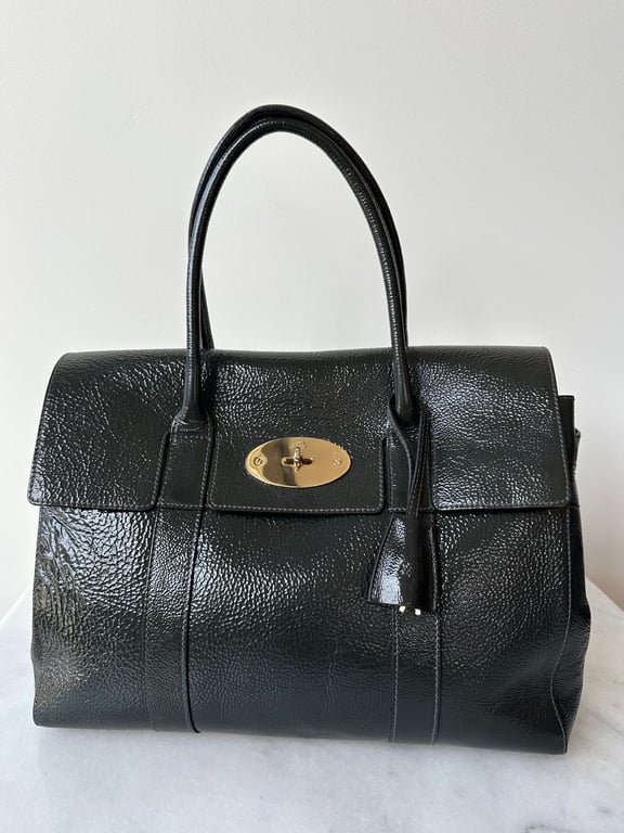 Sort lædertaske med to håndtag, struktur i materialet og en guldfarvet ovalt låsespænde foran.