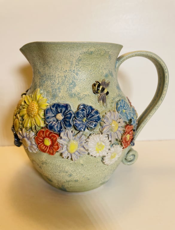 Keramikkande med relief af farverige blomster og en bi på en grønblå baggrund.