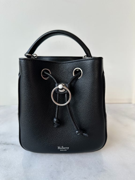 Sort Mulberry håndtaske i læder med snøre og metalring foran, stående på marmoroverflade.