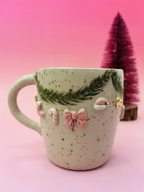 Krystalhvid keramikkop med julemotiver i pastelfarver mod lyserød baggrund med lilla juletræ i baggrunden. (1)