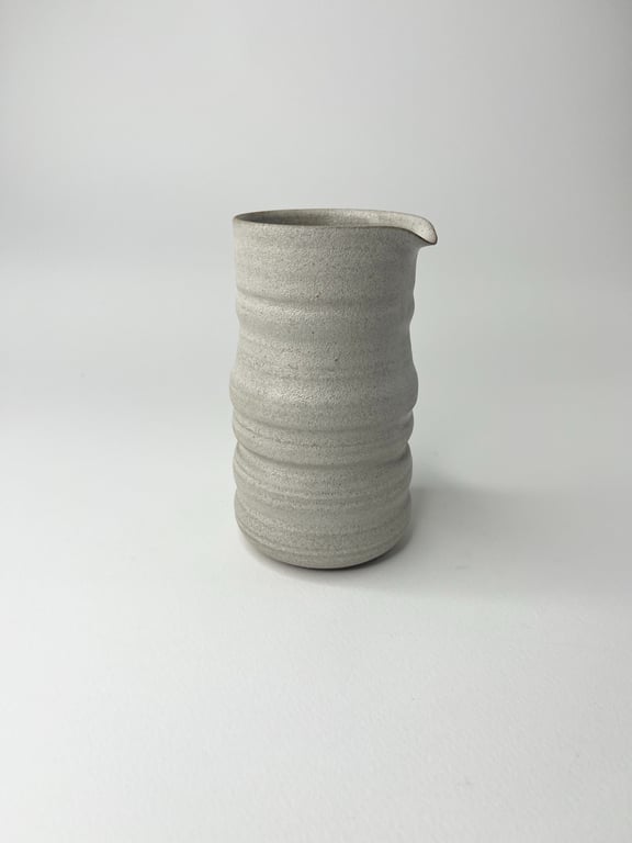 Grå keramisk kande med rillede detaljer og lille tud på hvid baggrund.