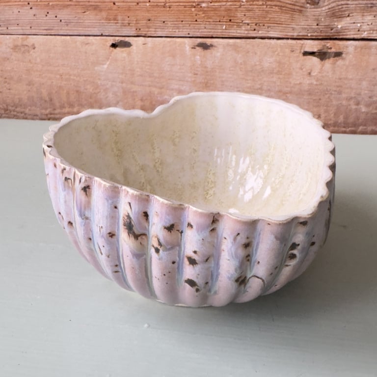 Keramisk, hjerteformet skål med bølget kant og udvendige riller, farvet i lyserøde og brune nuancer.