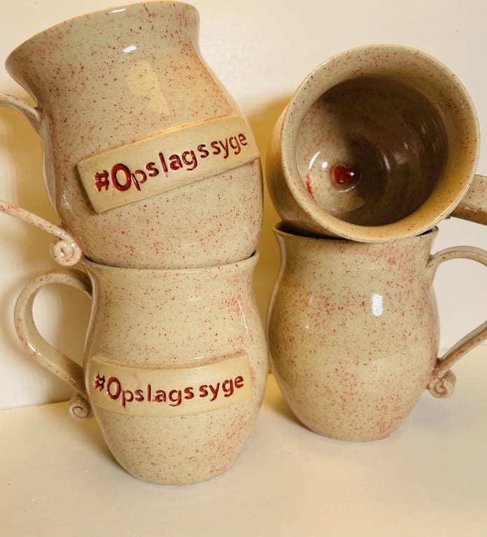 Billede af fire beige keramikkrus med røde prikker, hvoraf to har teksten "#Opslags syge" i rød skrift på den ene side.