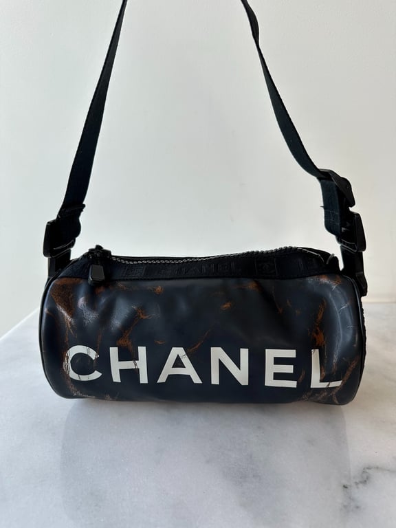 Sort Chanel skuldertaske med justerbar rem og hvidt logo, let brugsspor.