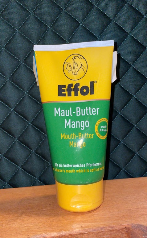 Tube med Effol Maul-Butter Mango mundsmørre til heste, stående på et træbord med mørkt quiltet stof i baggrunden.