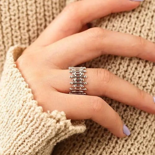 Hånd iført beige striksweater med sølvring med flere små stænger og kugledetaljer på ringefingeren. (3)