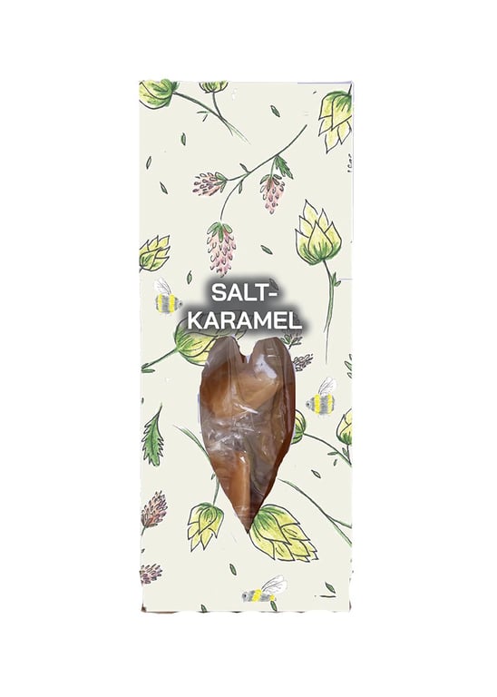 Indpakning med blomster- og bi-motiv med tekst "Saltkaramel" og transparent hjerteformet vindue, der viser karamel inde i pakken.