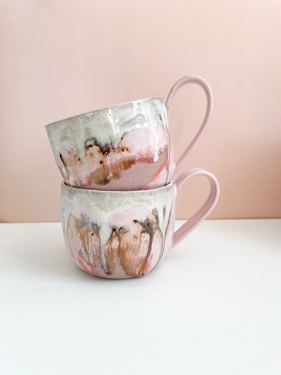 To keramik krus med abstrakt, pastel farvet glasur i rosa, beige og brun, stablet mod en lyserød baggrund.