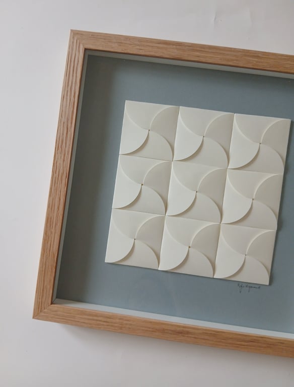 Indrammet kunstværk bestående af 12 hvide, buede firkantede elementer arrangeret i et 3x4 mønster på en grå baggrund.