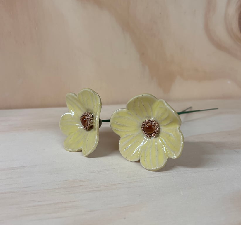 To keramiske gule blomster med brun midte på en lyse træflade.