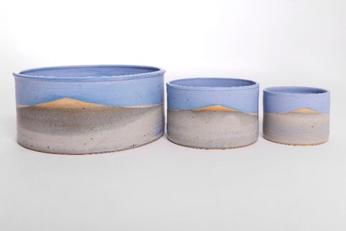Tre runde keramikskåle med håndmalede landskabsbilleder af sand, hav og himmel, fra størst til mindst række.