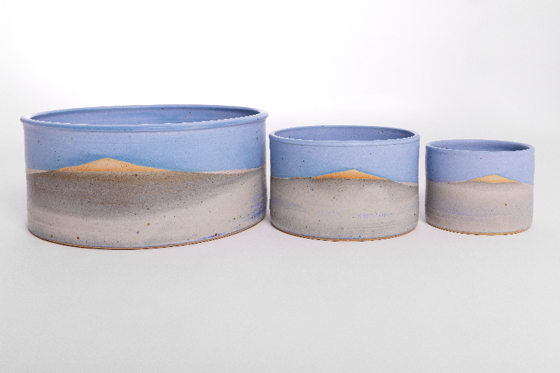Tre runde keramikskåle med håndmalede landskabsbilleder af sand, hav og himmel, fra størst til mindst række.
