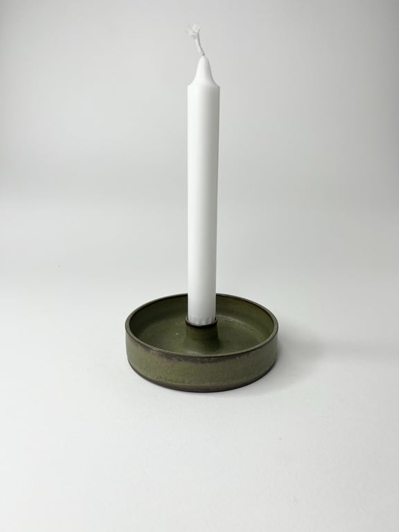 En hvid, ubrugt stearinlys i en rund, grønmetal candlestand.