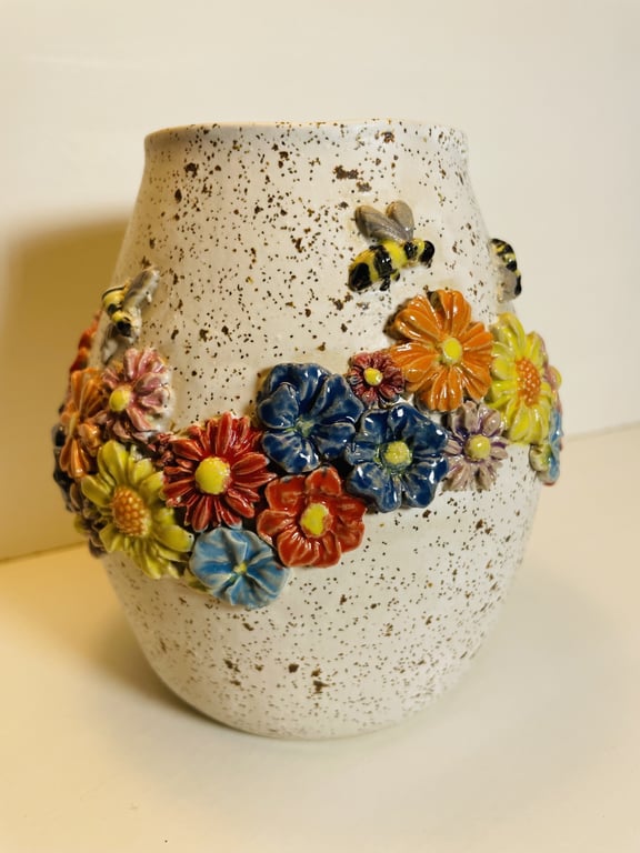 Hvid keramikvase med brunlige prikker, dekoreret med farverige blomster og bier i relief rundt om midten.