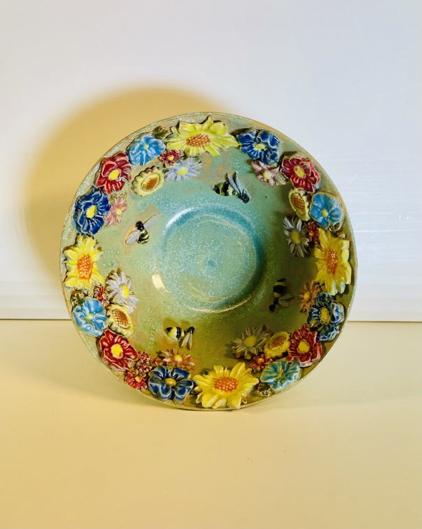 Keramisk skål med glaseret grøn inderside udsmykket med farverige blomster og bier langs kanten.