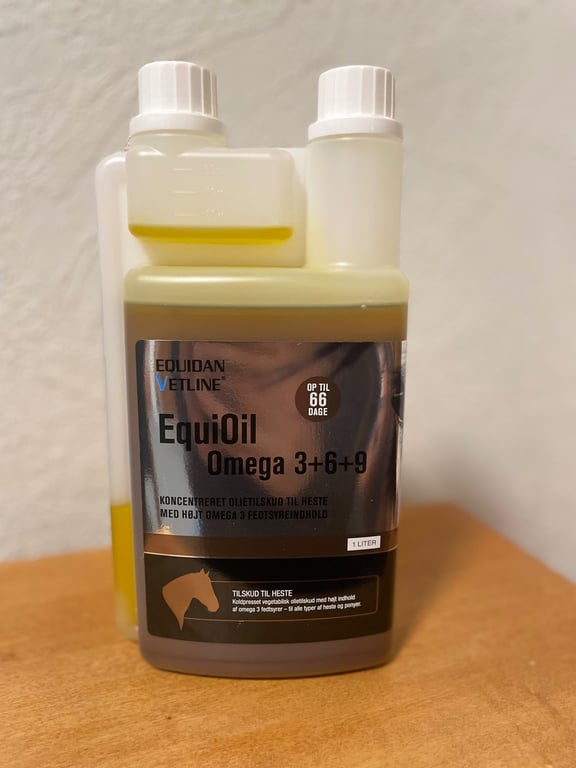 Flaske med EquiOil Omega 3+6+9, et koncentreret olietilskud til heste med højt omega 3 fedtsyreindhold, placeret på en træbordplade.