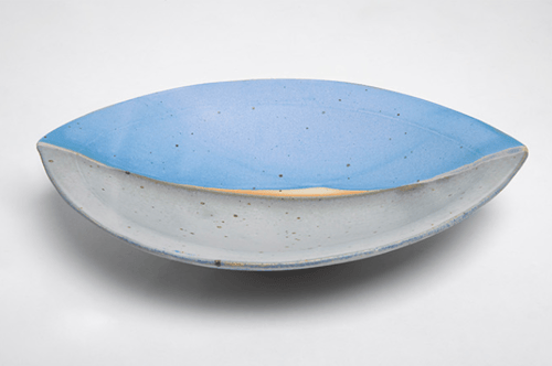 En oval skål med blå inderside og en lys, let røgfarvet yderside står på en hvid baggrund.