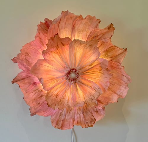 Lyserød og orange blomsterlampe med bløde, bølgede kronblade, der udsender et varmt, diffust lys mod en lys væg. (1)