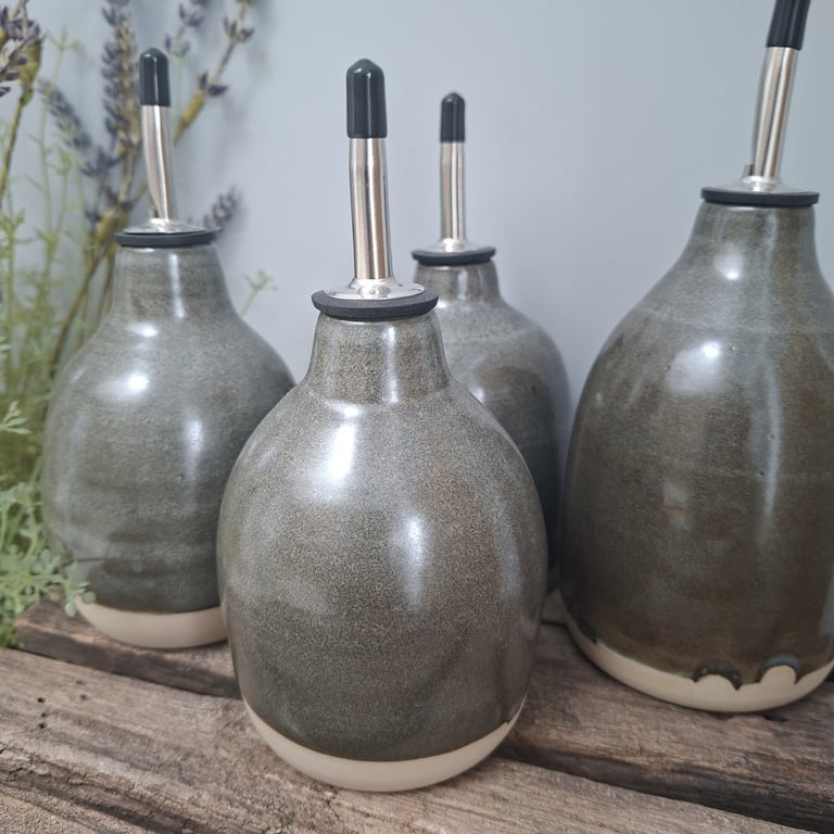 Fire grå keramikflasker med metalstuds på toppen, placeret på rustikt træbord med afdæmpet baggrund og lidt tørret lavendel til venstre.