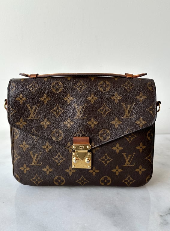 Brun Louis Vuitton håndtaske med ikonisk monogrammønster og gyldent spænde, placeret på hvid baggrund.