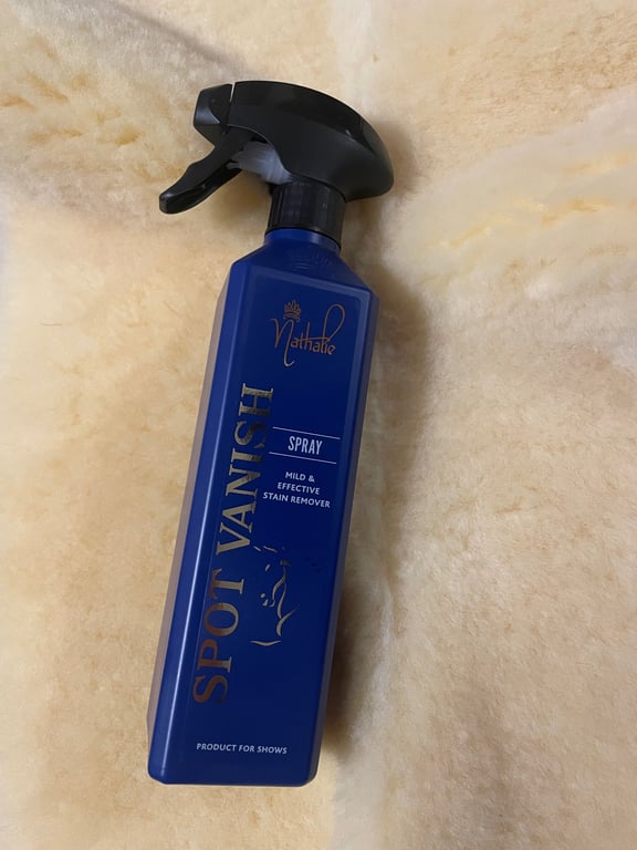 Flaske med blå Spot Vanish pletfjerner spray liggende på en lys pels eller blødt stof.