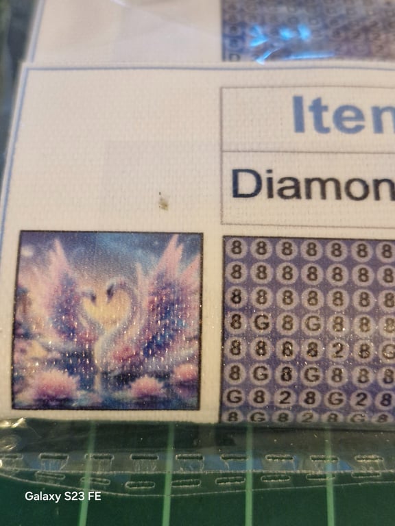 Nærbillede af et diamantmaleri kit med et glitrende billede af to svaner, der danner et hjerte med deres næb.