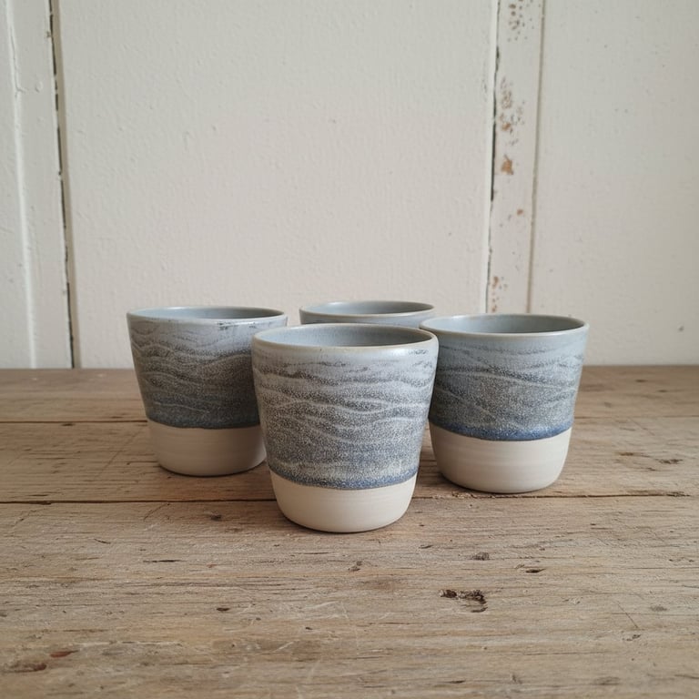 Fire keramikkrus med blågrå glasur øverst og ubehandlet hvid bund, placeret på et rustikt træbord foran en hvid væg.