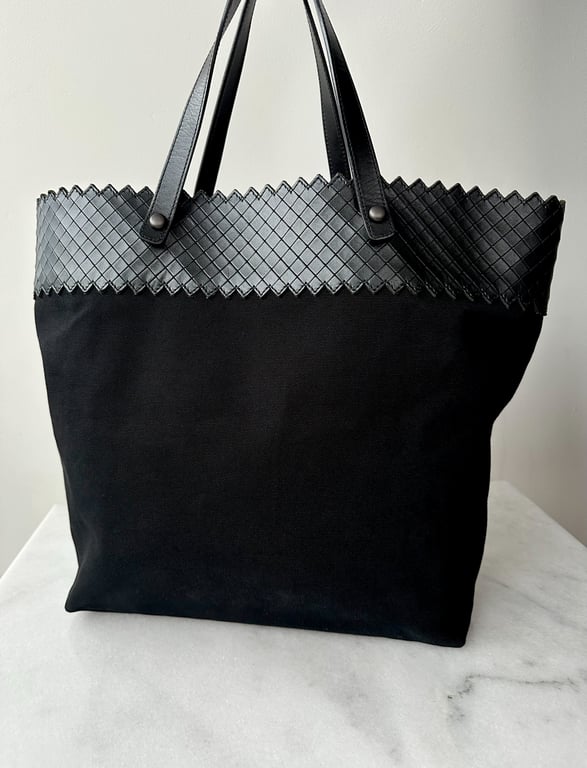 Sort tote-taske med vævet øverste kant og to sorte håndtag, placeret på en hvid marmorbordplade.