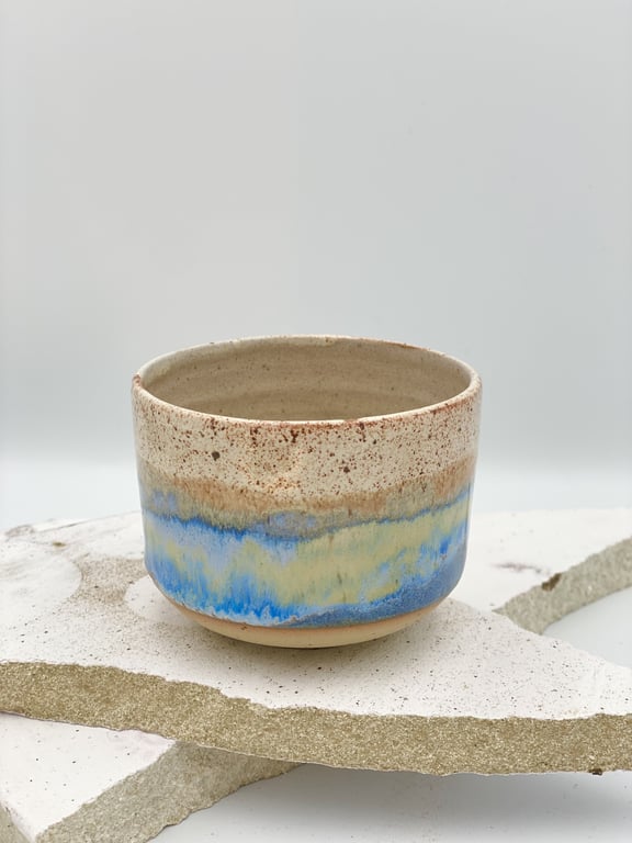 Keramisk kop med beige, blå og lysegule nuancer placeret på brudte stykker af hvidt og beige stenmateriale.