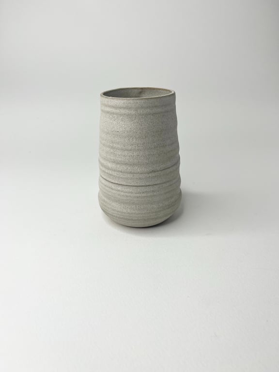 Grå keramisk kop med bølgede riller på hvid baggrund.