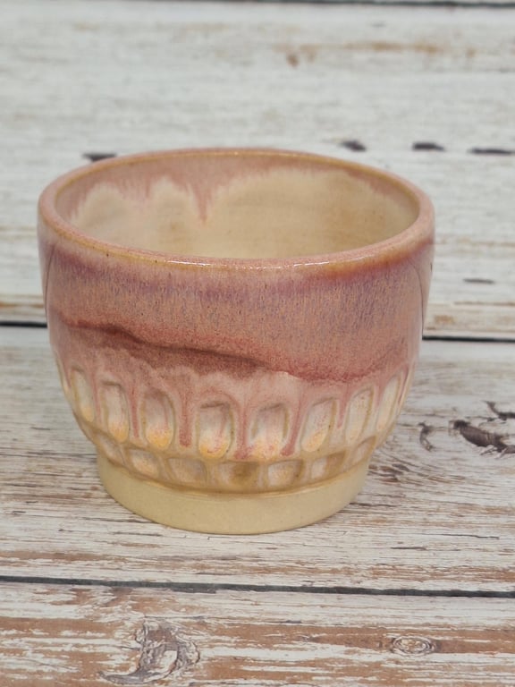 Lille keramikskål med beige og rosa glasur placeret på en hvid træoverflade.