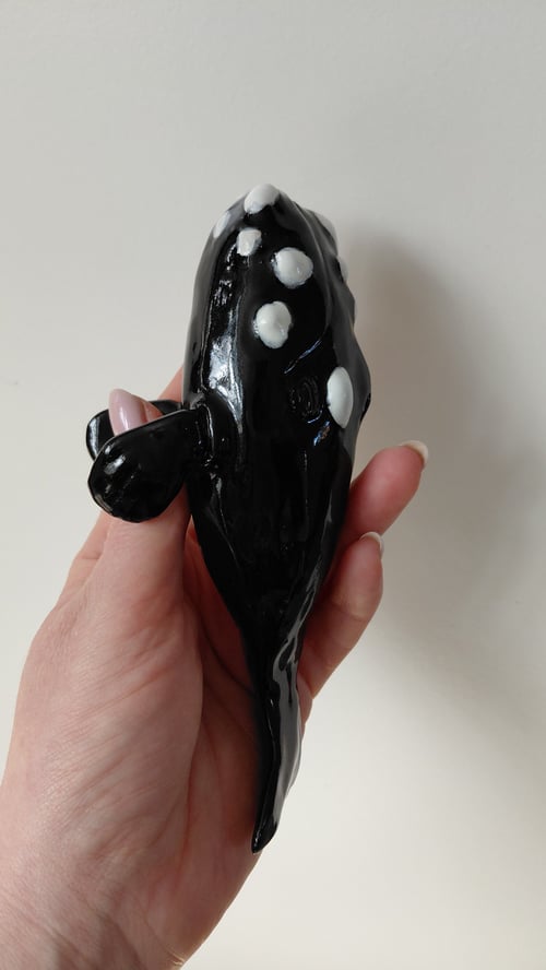 En hånd holder en sort keramikfigur formet som en hval med hvide prikker. (6)