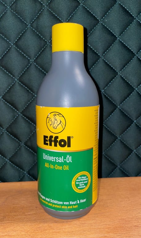 Flaske med Effol Universal-Öl All-In-One Oil til hud og hår plejefor heste og kæledyr, placeret på en træflade med mørk quiltet baggrund.