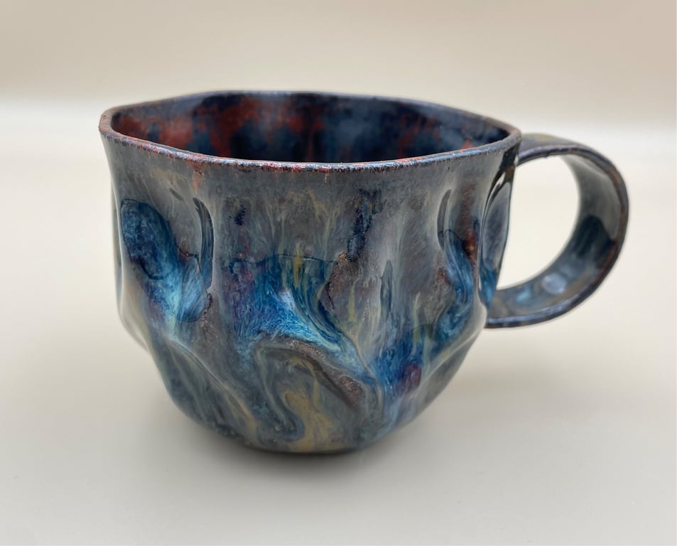 Keramisk kop med håndlavet, bølget overflade og blå, grå og lilla glasur.