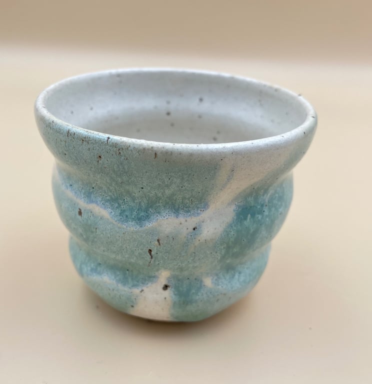 Lille keramisk kop med bølget form i hvid og blå glasur.