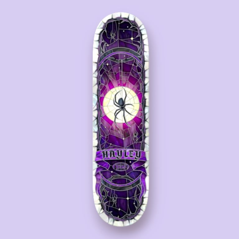 Skateboard deck med violet og sort farvetema, der viser et spindelvæv med en stor sort edderkop foran en gul cirkel, omgivet af mindre edderkopper og teksten "Hayley".