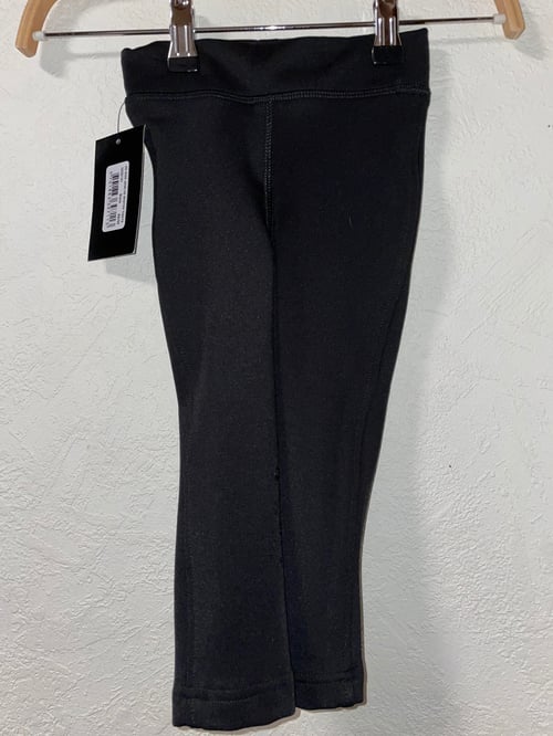 Sort leggings med elastisk talje hængende på en træbøjle mod en hvid væg, med en prismærke fastgjort. (1)