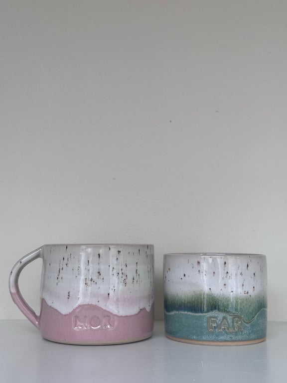 To kopper i keramisk materiale med glaseret overflade; den ene lyserød og den anden grøn, begge med hvide og brune nuancer, placeret på en hvid overflade mod en neutral baggrund.