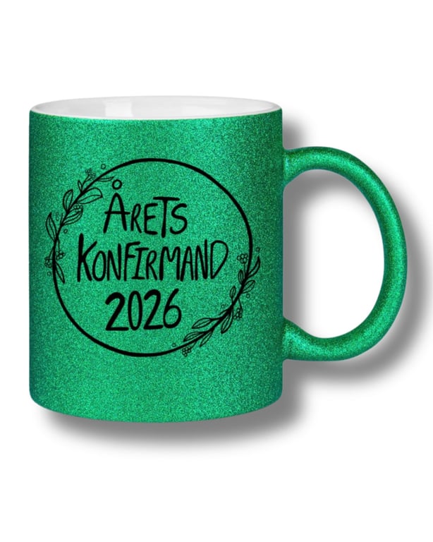 Grøn glitrende kaffekop med sort tekst og dekorativ krans, der siger "Årets konfirmand 2026".