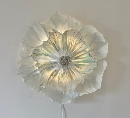 Billede af en hvid blomstet væglampe med bløde, lagdelte kronblade, der udsender et varmt lys. (1)