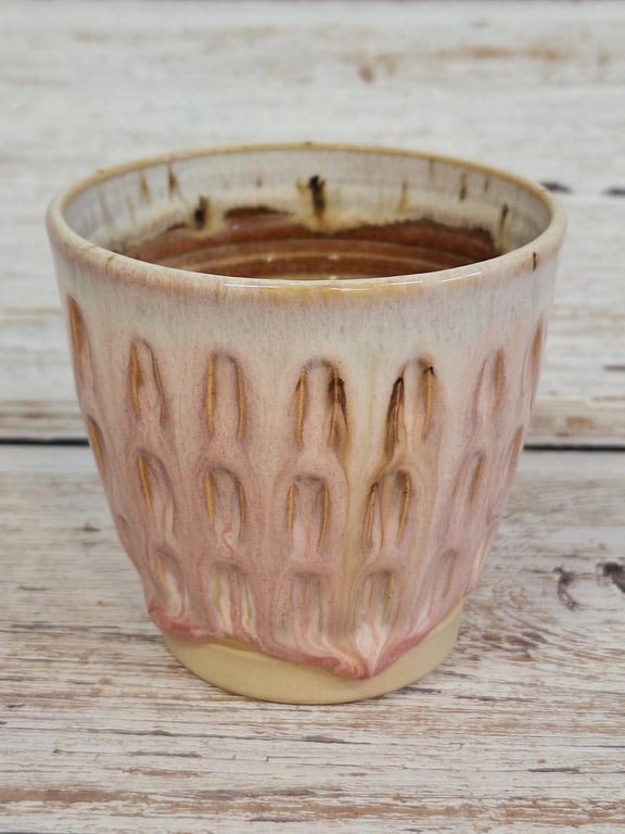 Keramikkrus med en tekstureret, rødlig og beige glasur, placeret på en træoverflade.